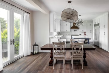 Dinning area in a living room. A floor to ceiling glass doorway with retractable curtains by the side and kitchen in the background