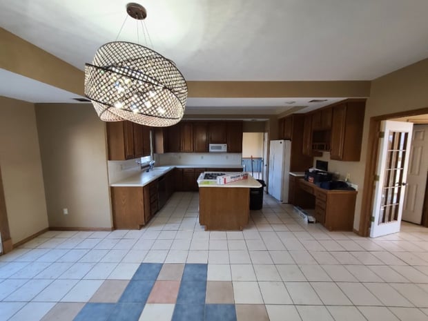 Empty traditional kitchen with dark oak cabinets, basket cage chandelier, and multicolored vinyl floor before remodel