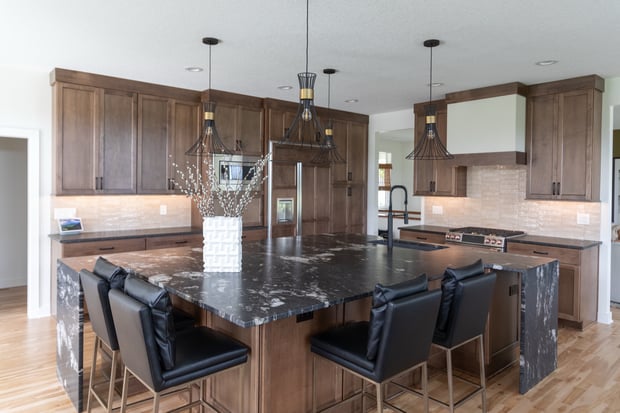 Open-concept main floor with stained wood kitchen cabinets, black granite waterfall island, and geometric pendants