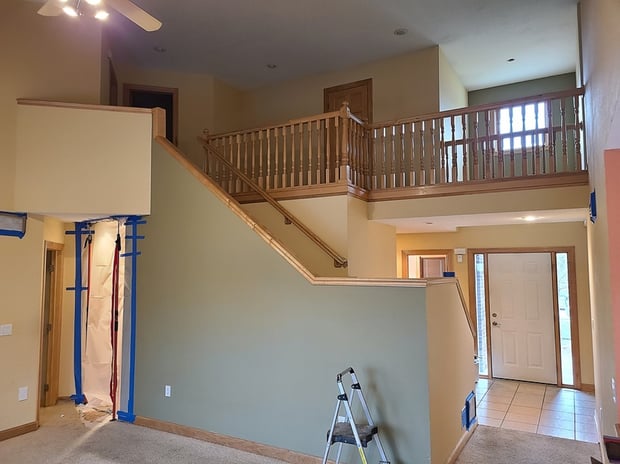 Dated two-story foyer with carpet, oak railings, beige walls, and tile entry before remodel