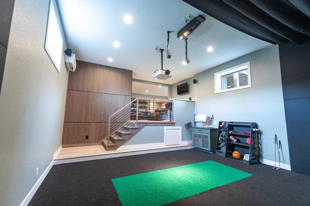 High-end home gym and golf simulator addition with putting turf, projector, and equipment storage