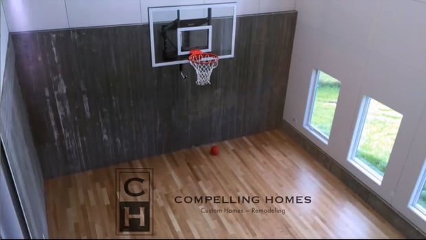 Indoor sport court addition with basketball hoop, dark wood feature wall, and large windows