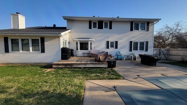 Exterior view of white two-story home with gray shutters and existing wood deck before addition
