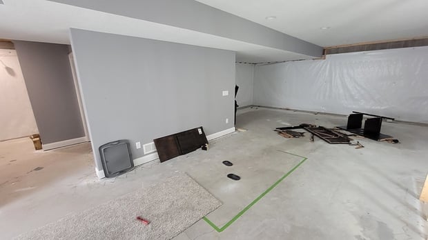 Unfinished basement with bare gray walls, exposed concrete floor, and plastic sheeting before bar build