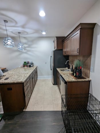 Galley-style basement kitchenette with cherry cabinets, granite counter, and basic pendant lights before remodel