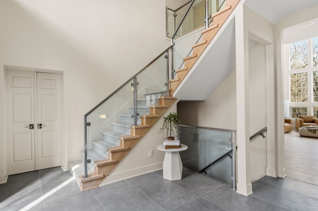 Modern open staircase with light wood treads, glass railings, and tile-floor landing