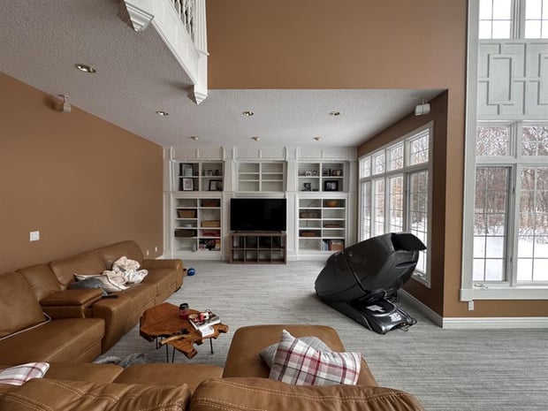Two-story living room with white painted built-ins, dated brown walls, and basic carpet before remodel