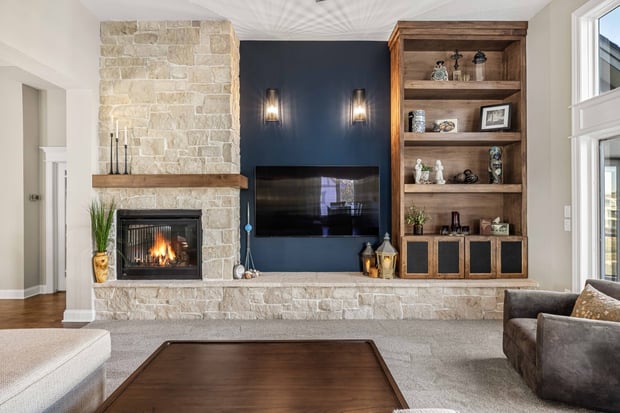 Modern living room with stacked stone fireplace, navy accent wall, wood mantel, and built-in shelving